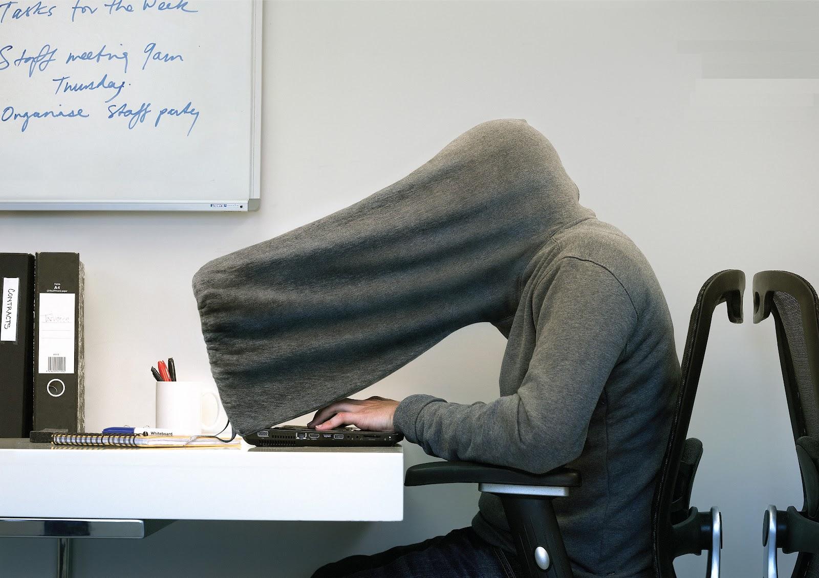 A hacker in a hoodie that covers their head and computer screen